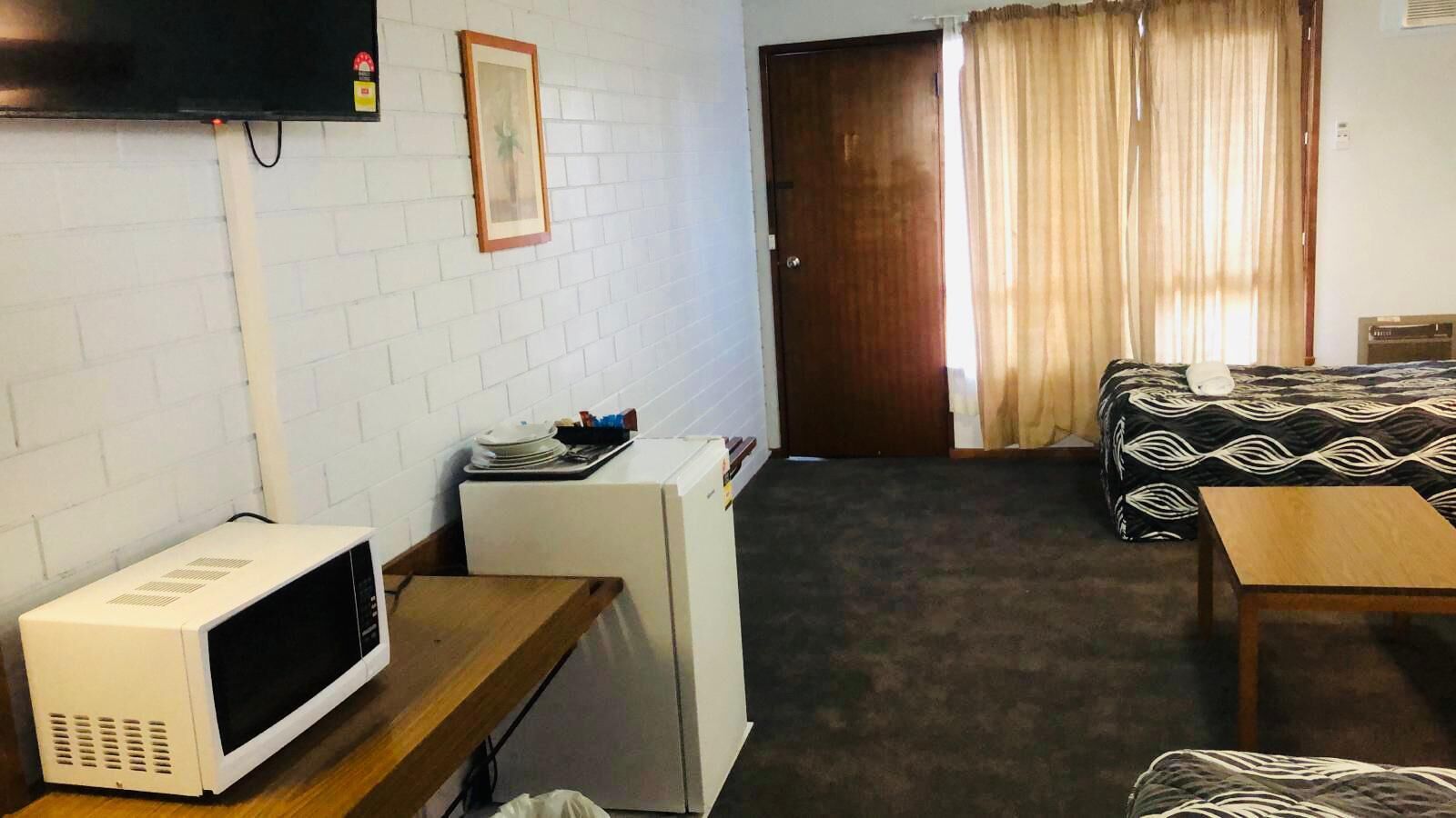 Ein gemütliches Hotelzimmer mit Küchenzeile, einem Bett mit gemusterten Textilien, einem Holztisch und einem an der Wand montierten Fernseher.