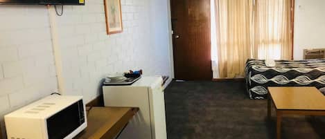 Ein gemütliches Hotelzimmer mit Küchenzeile, einem Bett mit gemusterten Textilien, einem Holztisch und einem an der Wand montierten Fernseher.