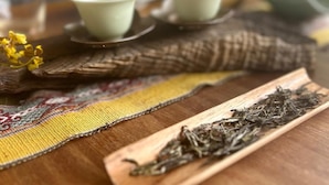 Ein Holztisch mit einer gewebten Tischmatte, einer Teekästchen mit Teeblättern und einem Satz grüner Teetassen und Untertassen.