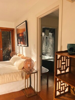 A bedroom with a bed, bedside table, and a view into a bathroom with a bathtub and shower. - Ecoasis Mami Wata Retreat (Smiths Creek)