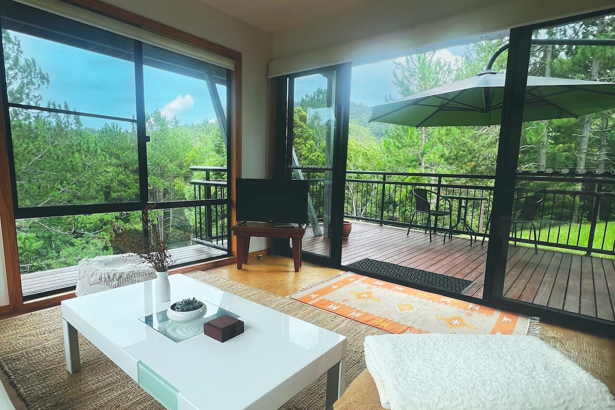 A modern living room with a white sofa, a coffee table, and a balcony with a view of greenery.