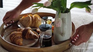 Ein Tablett mit Croissants, einer Kaffeekanne und einer Vase mit Blumen.