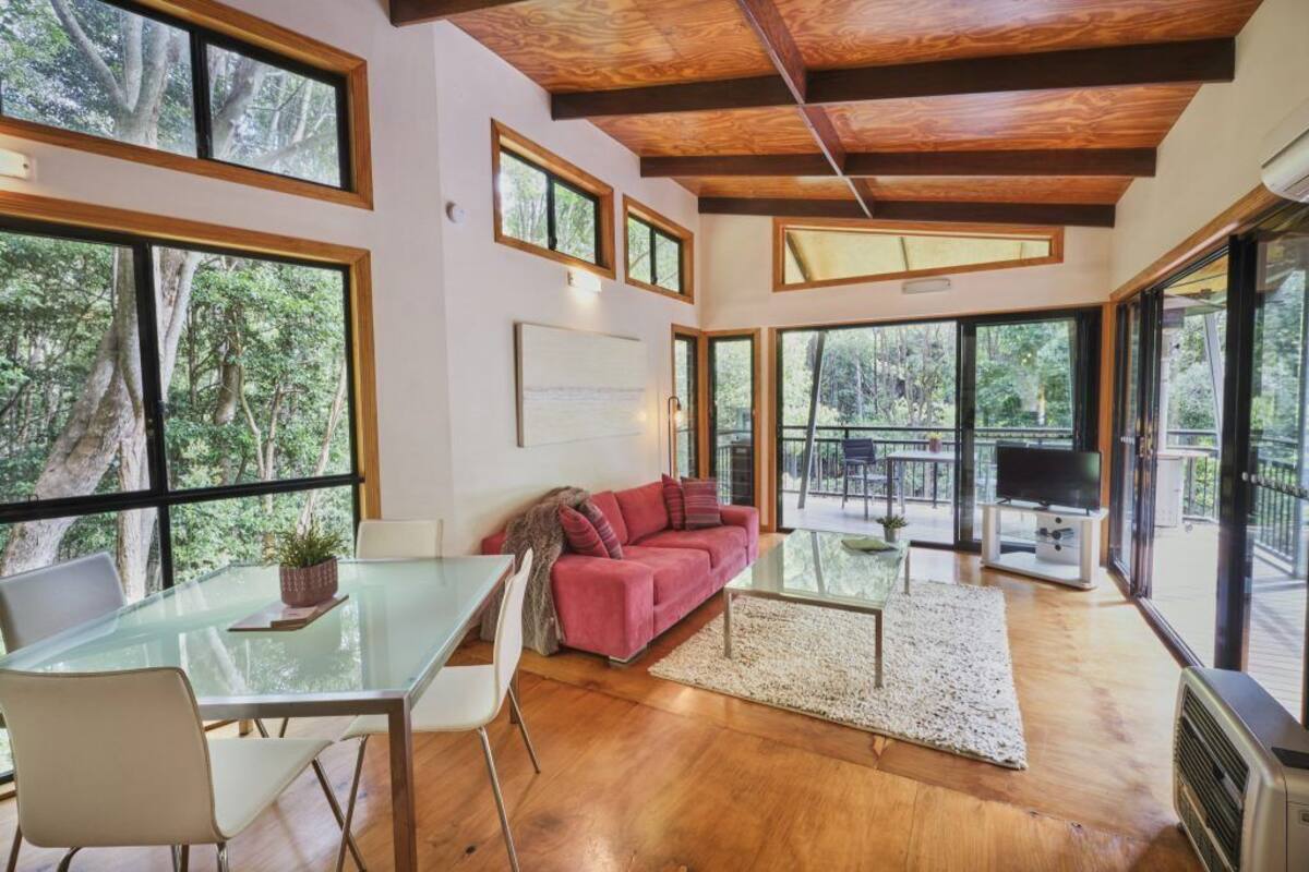 A spacious living area with a glass table, a red sofa, and large windows offering a view of the forest.