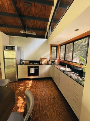 A compact kitchen with a microwave, refrigerator, and stove, wooden flooring, and a window providing natural light. - Ecoasis Mami Wata Retreat (Smiths Creek)