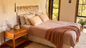 A bedroom with a bed, nightstand, and a window with a view of greenery.