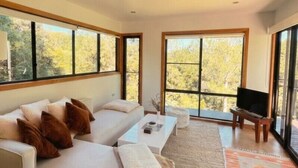 A modern living room with a sofa, a television, and large windows.
