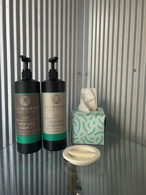 Two bottles of Evergreens organic hair care products, a tissue box, and a glass on a reflective surface.