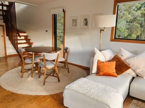 Una sala de estar con una mesa redonda de madera, un sofá blanco y una escalera.