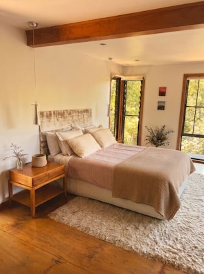 Un dormitorio con cama, mesita de noche, ventana y vistas a árboles.