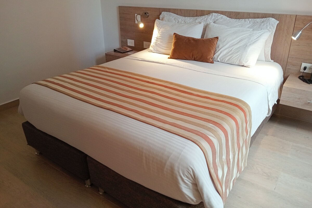A neatly made bed with a striped bedspread, a wooden headboard, and a bedside lamp.
