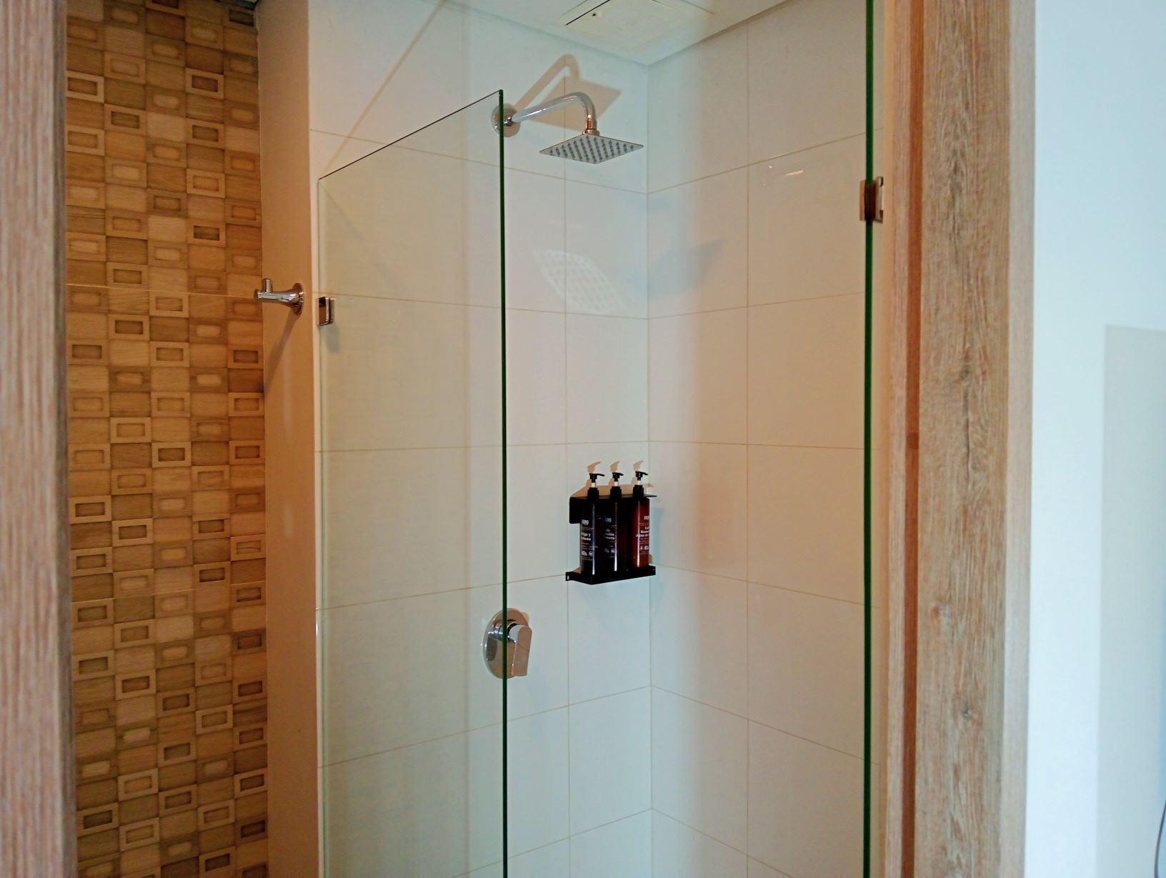 Ducha envuelta en vidrio con cabezal de ducha manual y repisa con artículos de aseo.