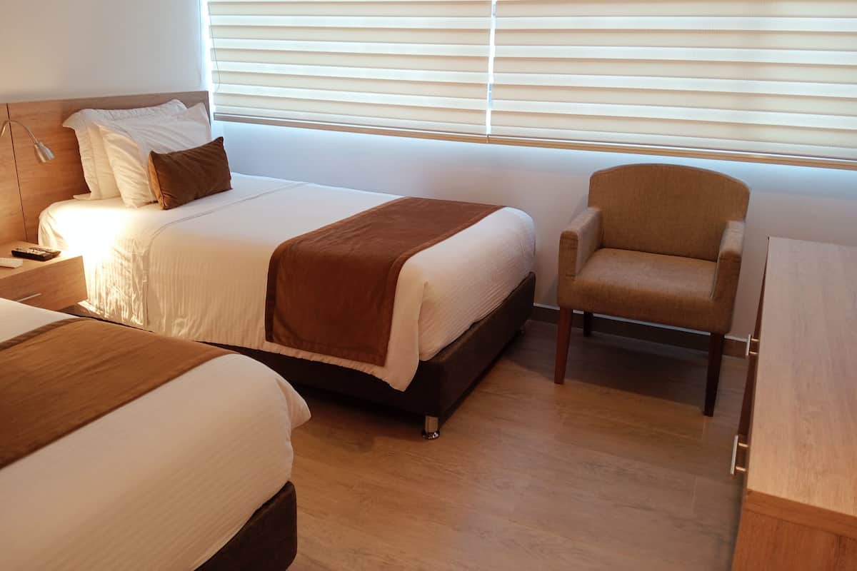 Una habitación de hotel con una cama grande, una cama más pequeña, una silla y un escritorio.