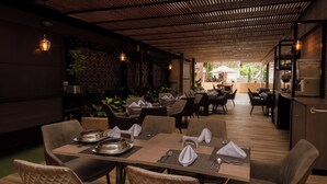 A restaurant with wooden tables and chairs, some with napkins and cutlery. There are plants and a view of the outdoors. - Hotel Lomas 10 (Medellín)