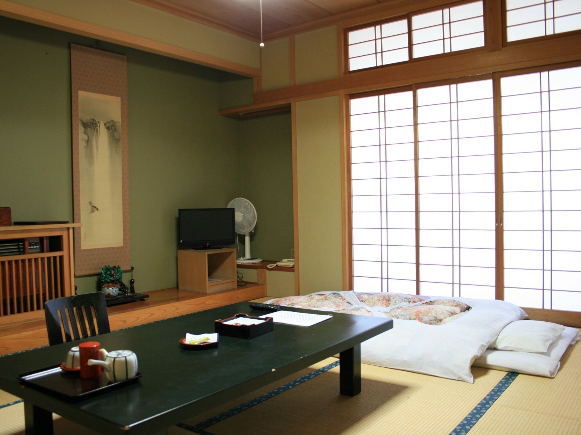 Une pièce de style japonais traditionnel, avec un sol recouvert de tatamis, une petite table basse avec un service à thé, un téléviseur et un lit équipé d’un futon.