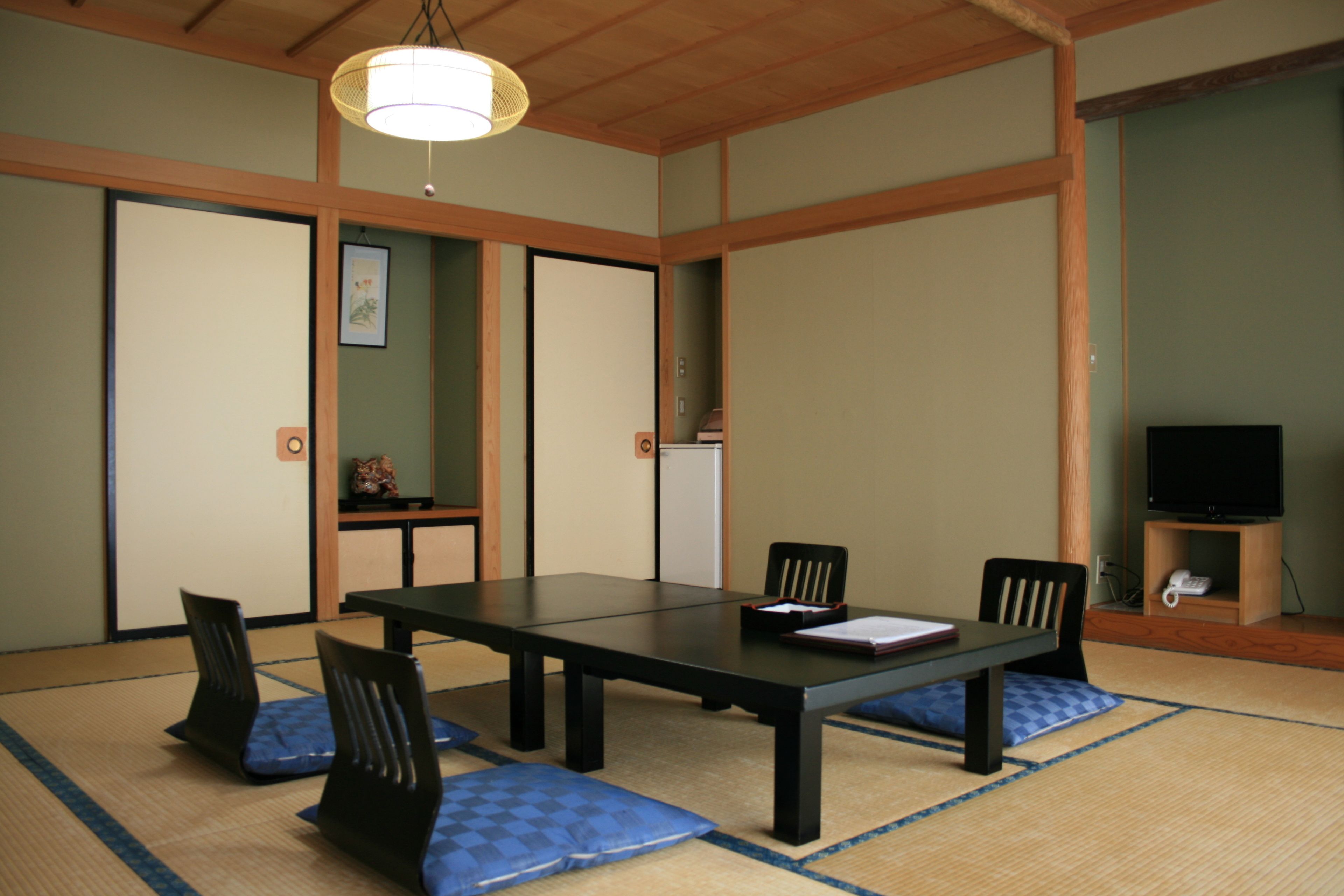 Una habitación japonesa tradicional con suelo de tatami, una mesa baja y sillas negras.