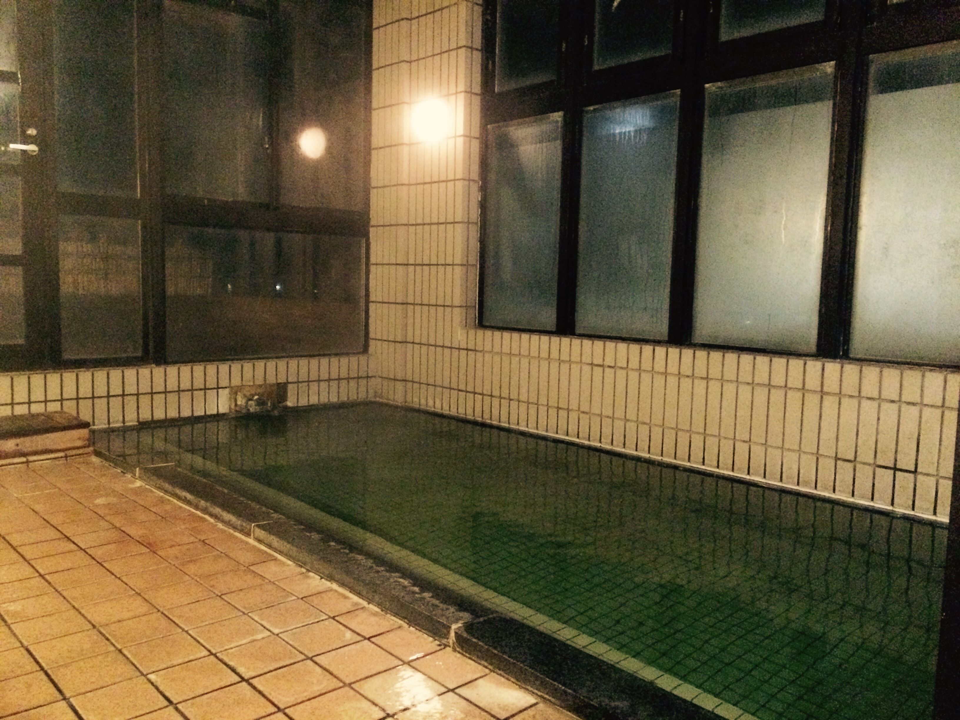 Un espace piscine carrelé, avec une surface d’eau claire, entouré de murs dont le revêtement est constitué de carreaux disposés en motif quadrillé.