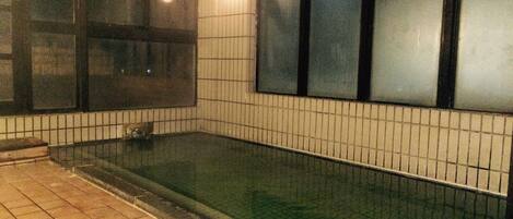 A tiled pool area with a clear water surface, surrounded by walls with a grid pattern of tiles.