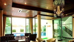 Un hall d'hôtel moderne avec vue sur la piscine, des fauteuils en cuir et un lustre.