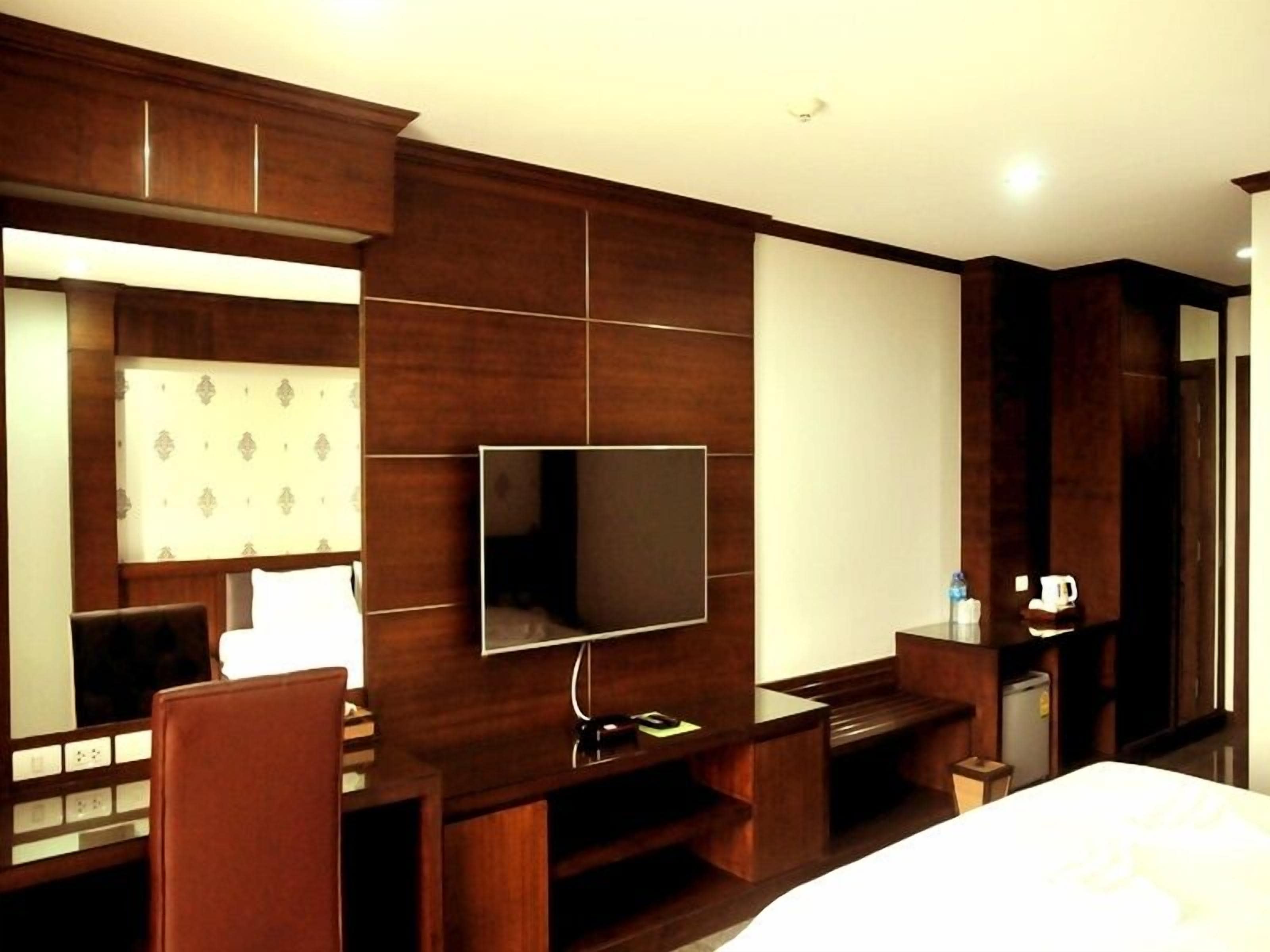 Habitación de hotel con un televisor de pantalla plana grande montado en la pared, un mueble de entretenimiento de madera, una cama y un pequeño escritorio con una silla.