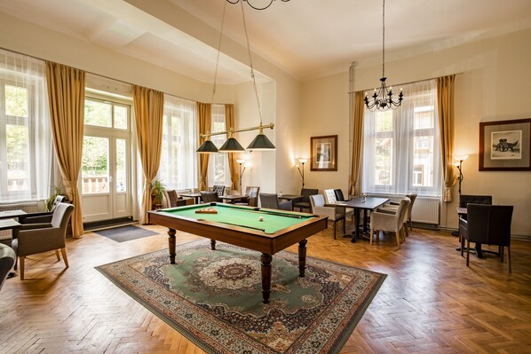 A spacious room with a pool table, comfortable seating, and large windows.