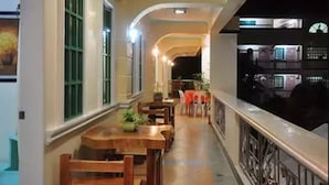 A corridor with wooden tables and chairs, a railing, and a view of a kitchen area. - Apartelle de Francesca (Puerto Galera)