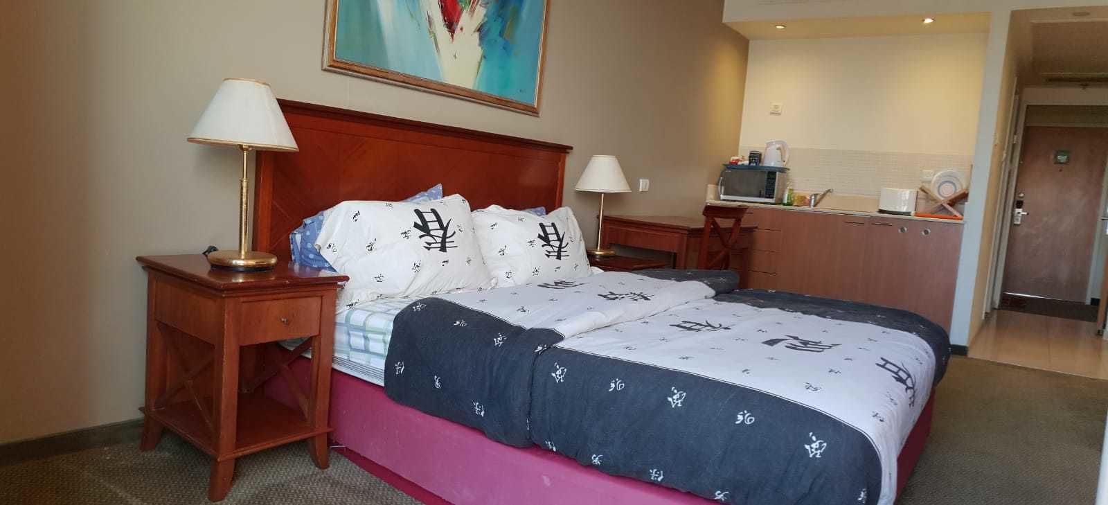 A hotel room with a bed, two bedside tables, a television, a microwave, and a kitchenette.