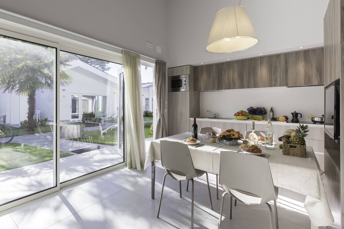 A modern kitchen with a dining area, large windows, and a view of the garden.