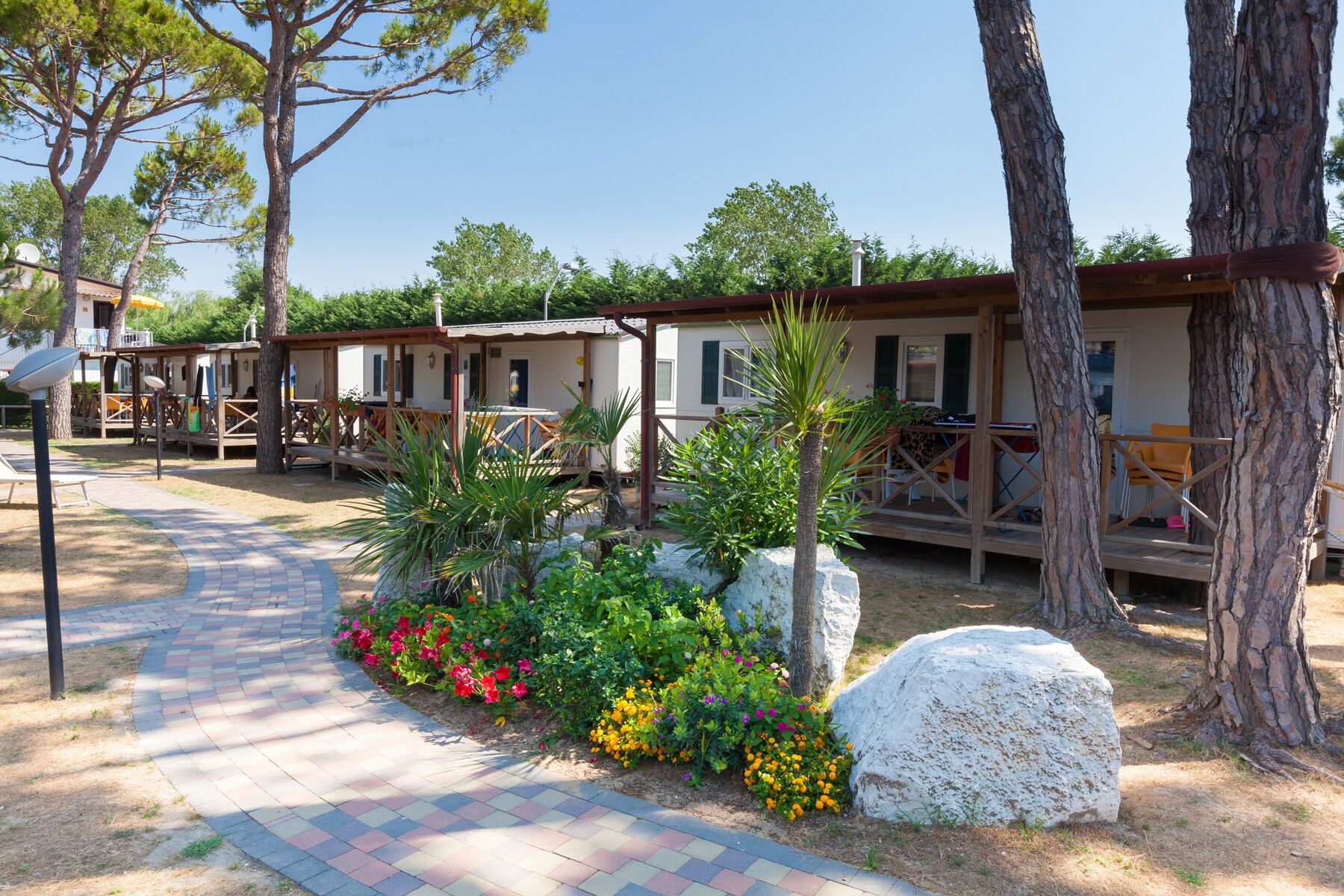 A row of wooden cabins with outdoor seating, surrounded by a garden with various plants and flowers.