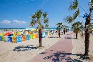 Ein Strand mit einer Holzstege, Palmen und bunten Strandstühlen.