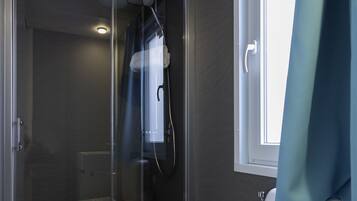 A modern bathroom with a glass shower enclosure, a bidet, a toilet, and a window with a curtain.