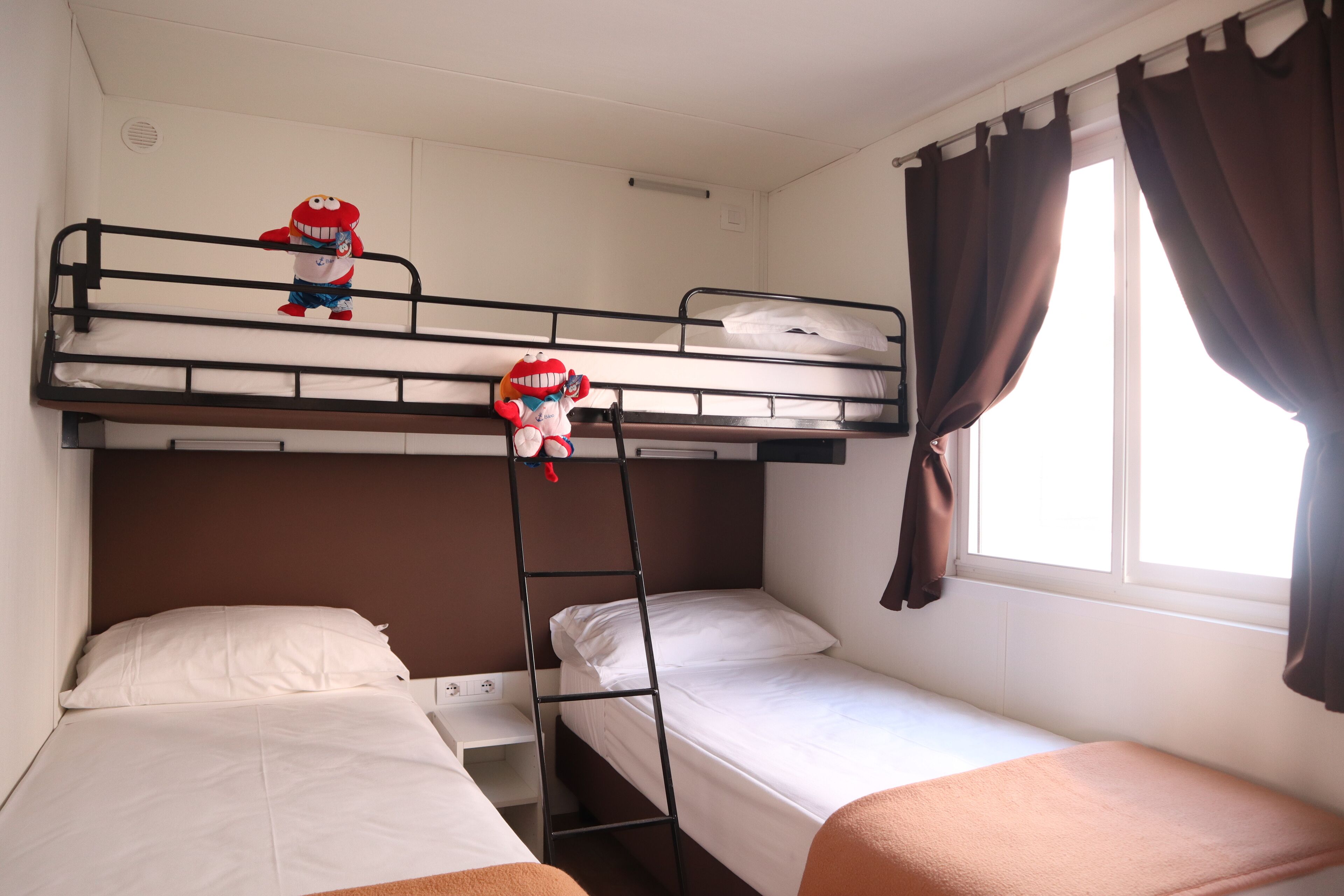 A bunk bed room with two beds, a ladder, and a window with curtains.