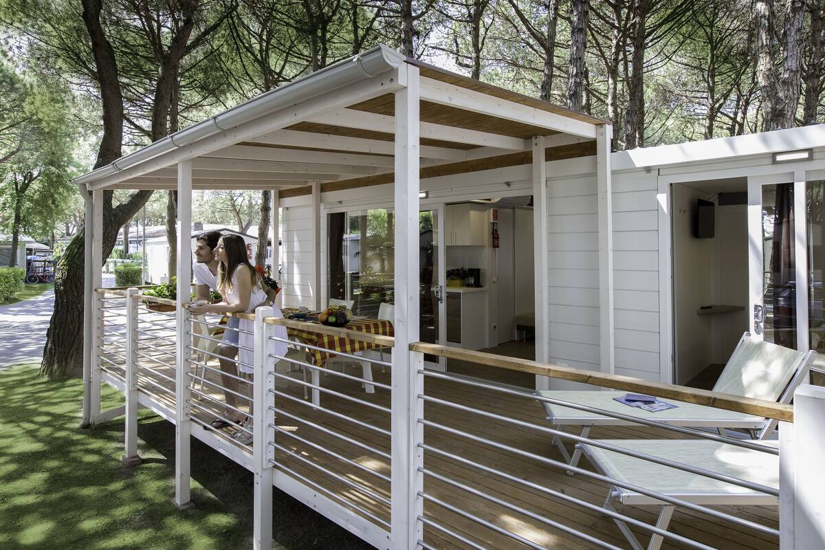 A covered outdoor area with a wooden deck, a table with chairs, and a small kitchen area.