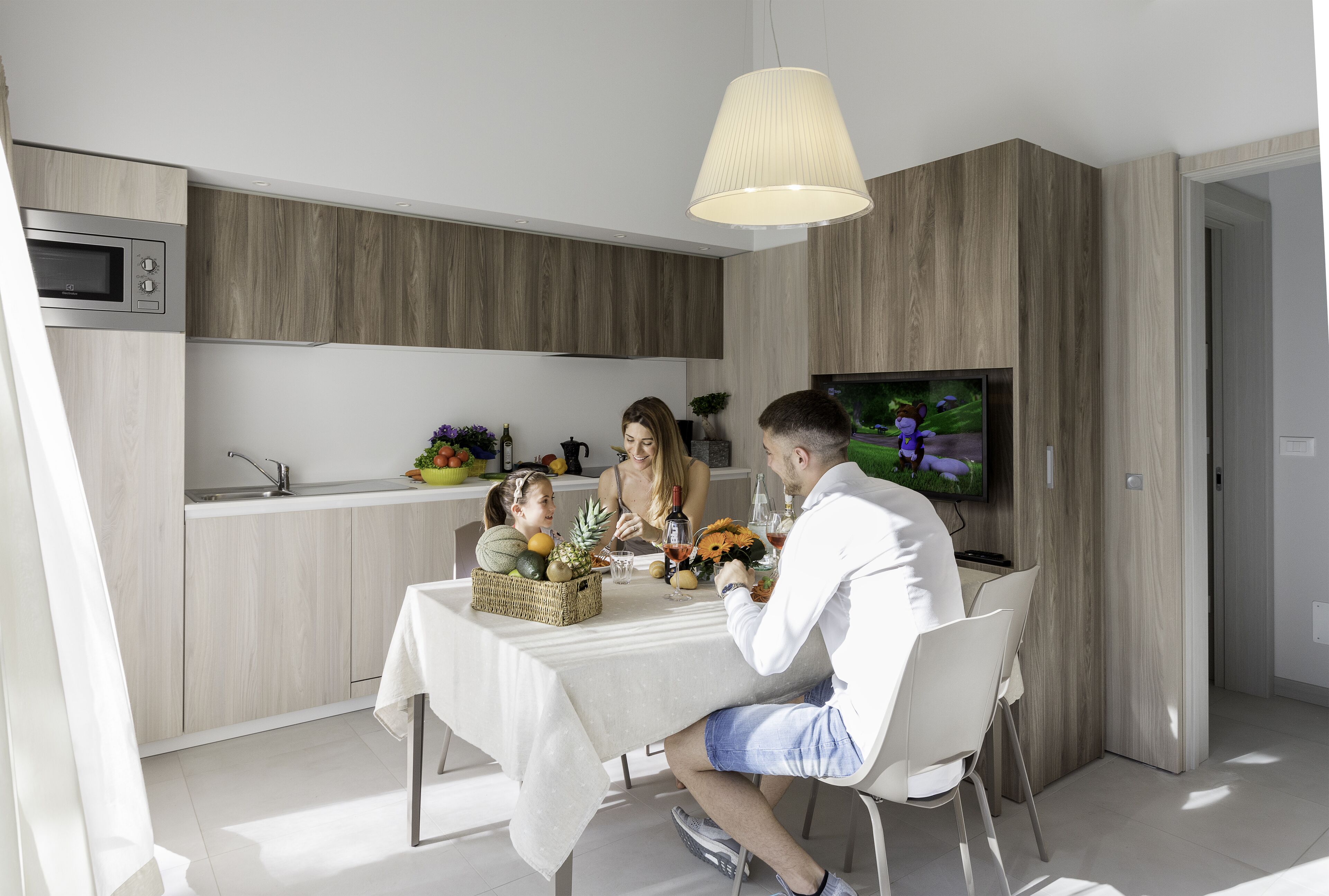 A modern kitchen with a dining area, a TV, and a wooden cabinet.