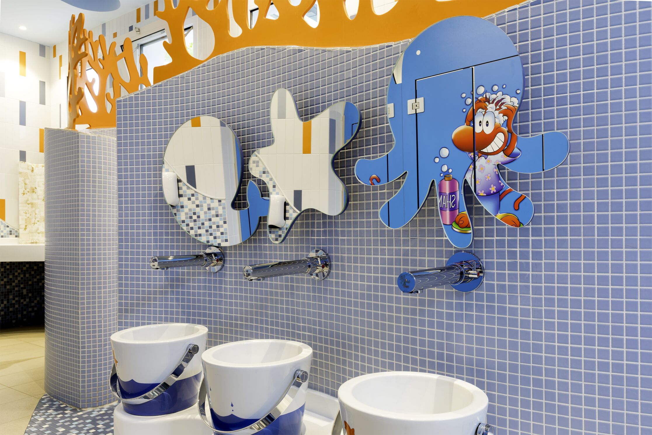 A bathroom with blue tiled walls, two sinks with white and blue fixtures, and a cartoon character decoration.