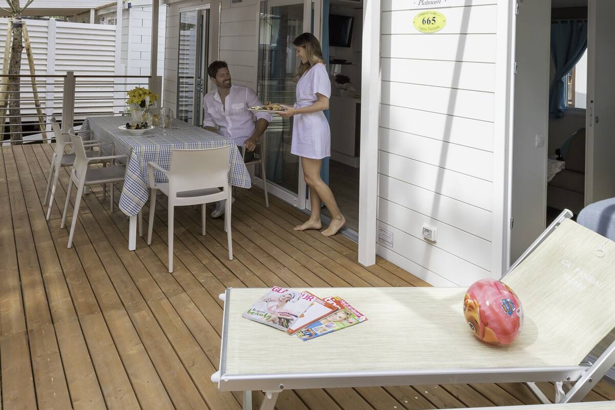 A covered outdoor area with a table and chairs, a covered seating area, and a sign indicating a room number.
