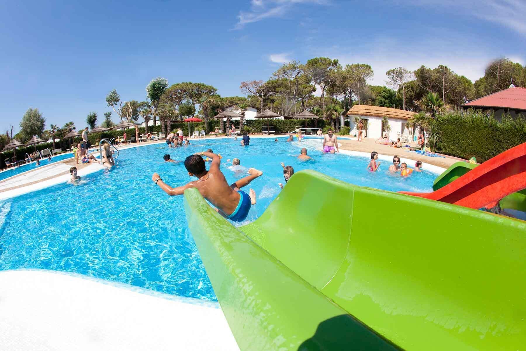 A swimming pool with a water slide, surrounded by palm trees and lounge chairs.