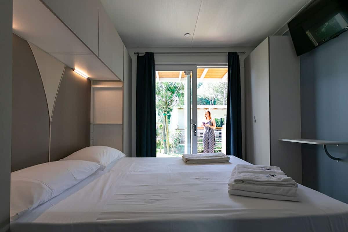 A hotel room with a bed, a TV, and a view of the outdoors.