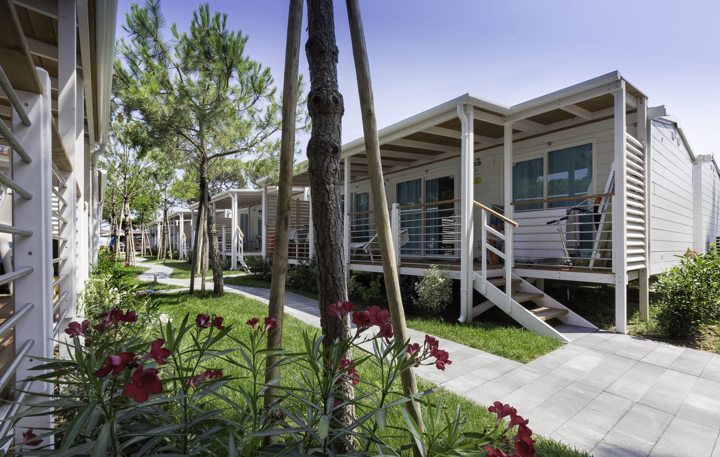 A row of modern, white cabins with balconies, surrounded by greenery and a clear sky.