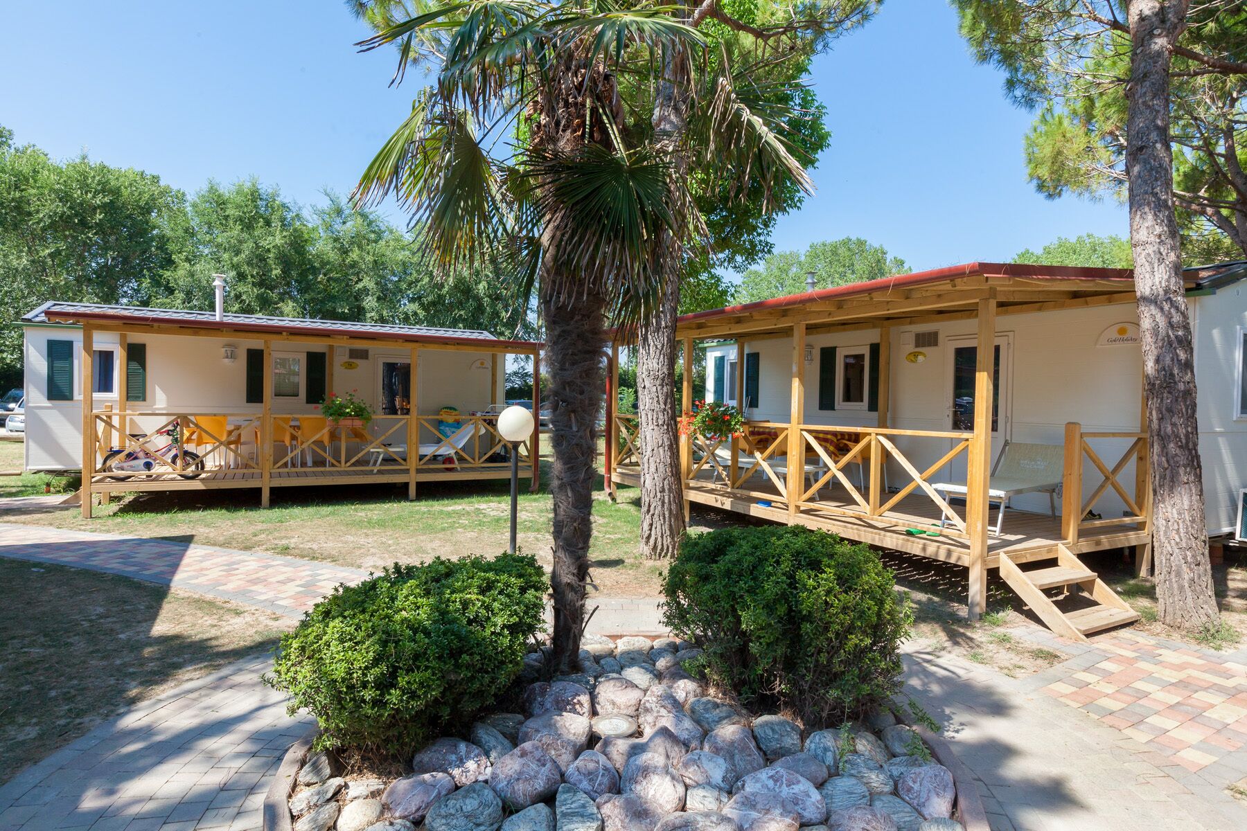 Two mobile homes with wooden decks, outdoor seating, and a paved walkway.