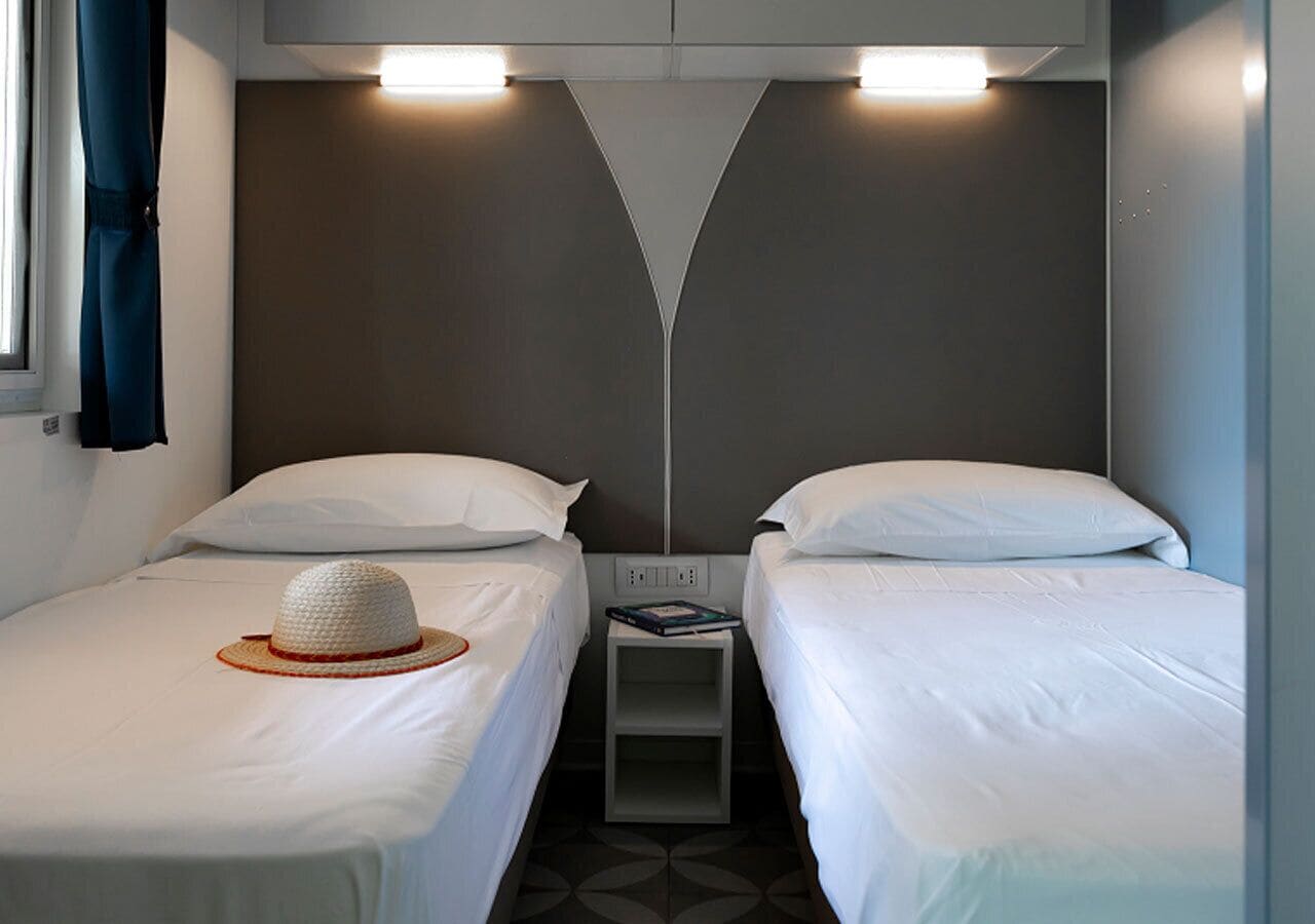 A hotel room with two single beds, a small bedside table, and a wall-mounted light fixture.