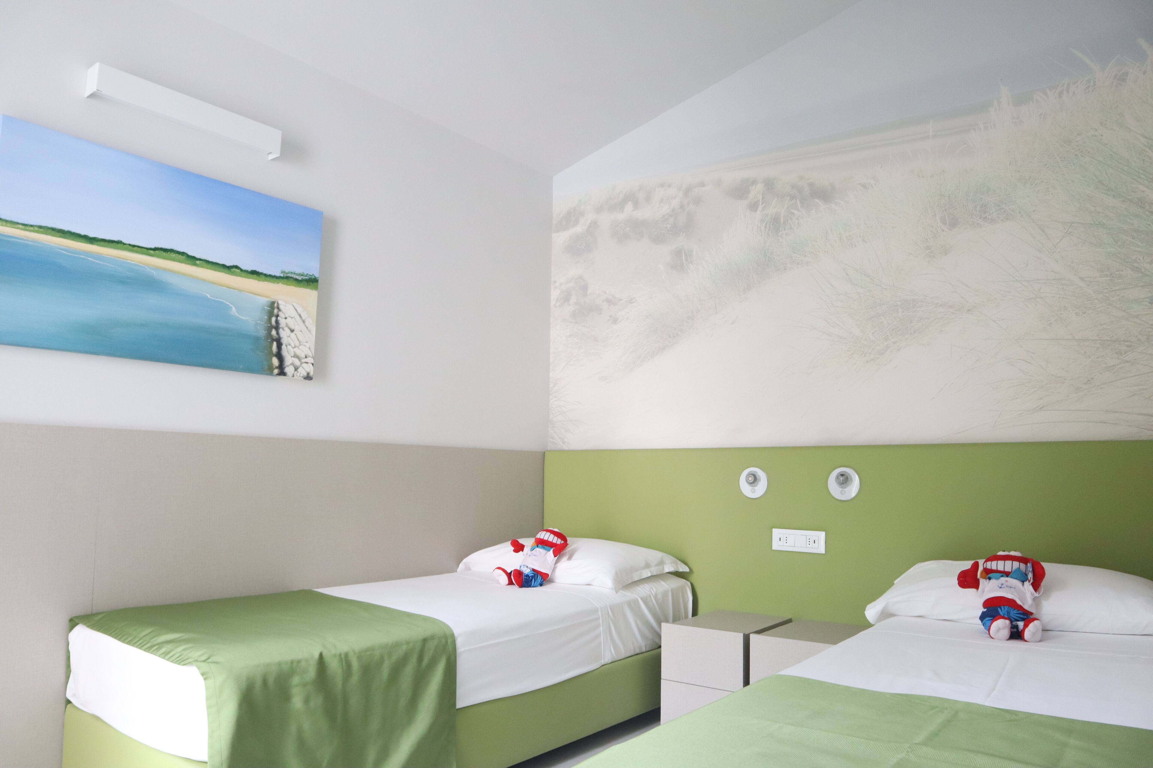 A hotel room with two beds, a nightstand, and a wall painting of a beach scene.