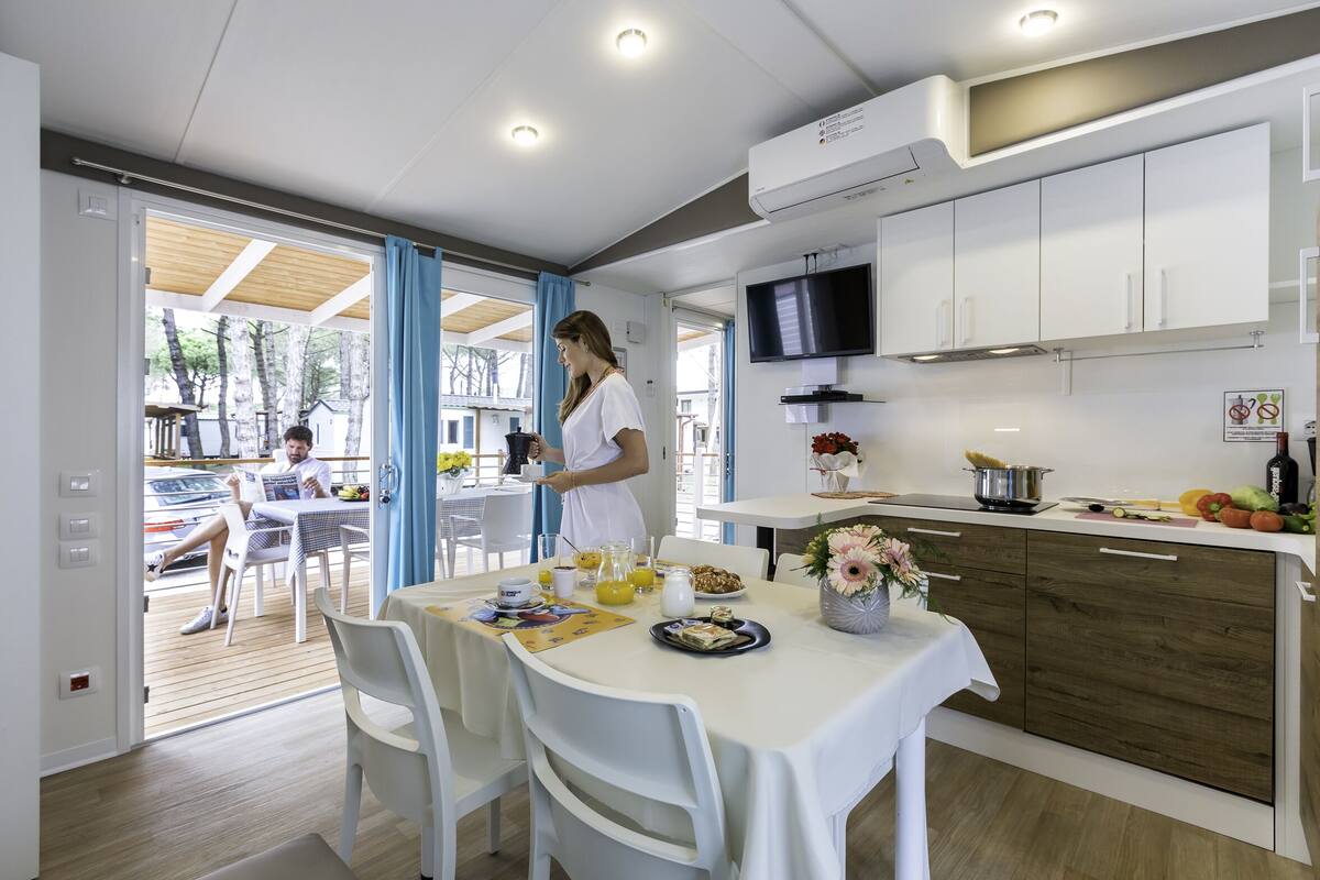A modern kitchen with white cabinets, a TV, and a dining area with a table set for breakfast.