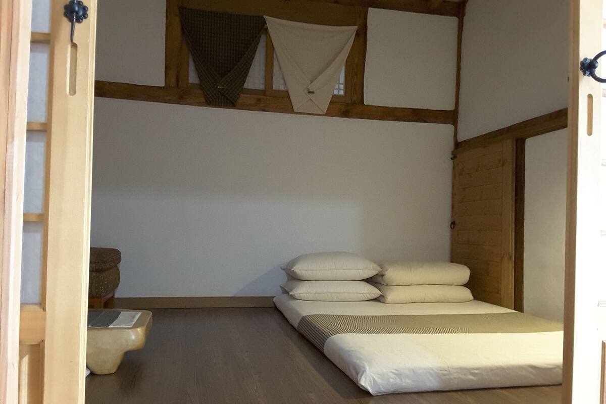 A minimalist room with a wooden floor, a bed with white bedding, and a small stone basin.