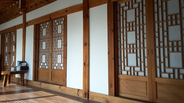 A traditional Japanese room with tatami flooring, wooden sliding doors with intricate lattice designs, and a wooden ceiling structure. - Yettle Hanok Stay (Gyeongju)