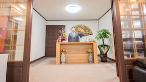 A reception area with a wooden desk, a fan, and a potted plant. - Hotel Kinwaso (Sapporo)