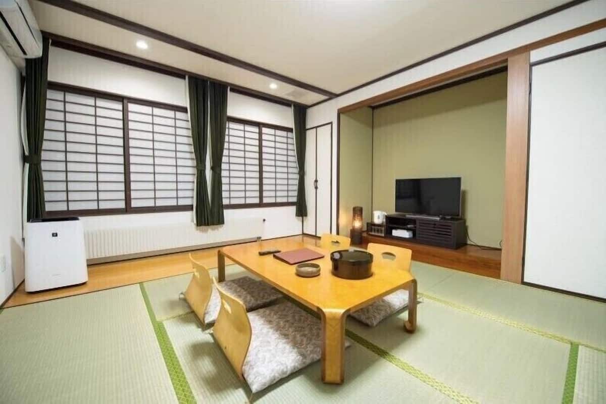 Um quarto japonês tradicional com tatames, uma mesa de madeira baixa, uma televisão e portas deslizantes.