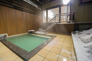 Baño de aguas termales con interior de madera, suelo de baldosas y una escalera que sube a un nivel superior.