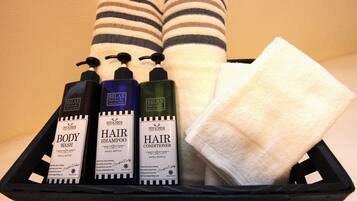 Ein schwarzes Tablett mit drei Nachfüllflaschen für Duschgel, Shampoo und Conditioner, zusammen mit zwei gestreiften Handtüchern.