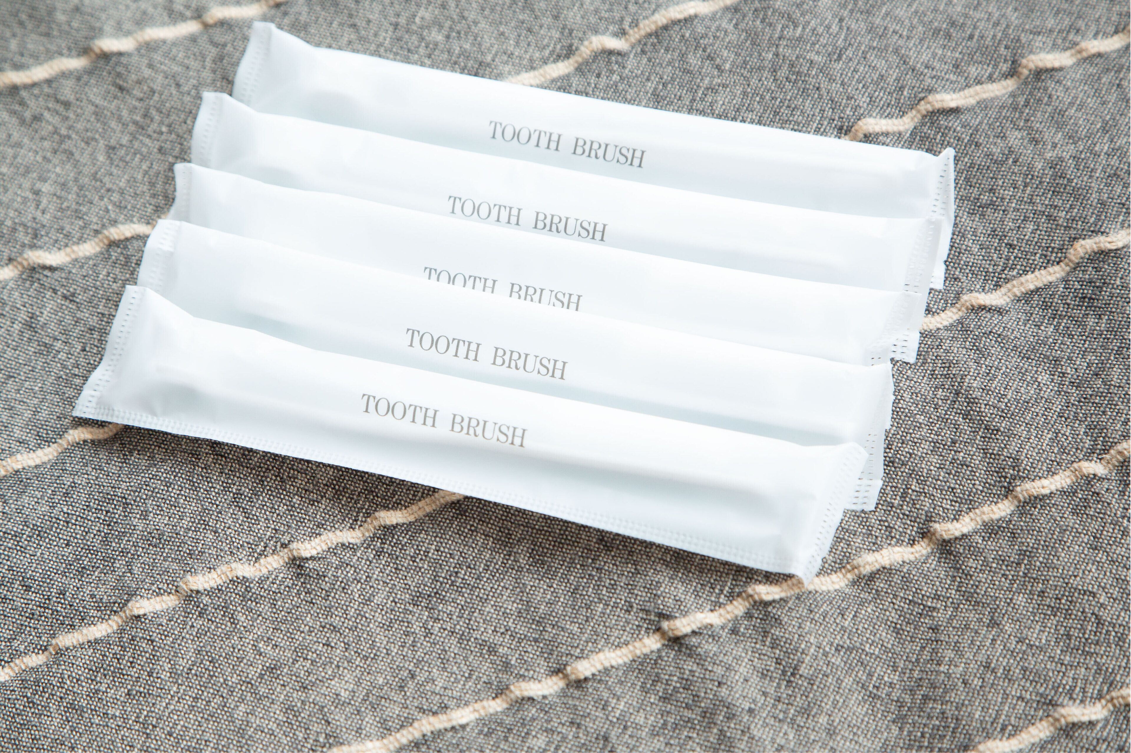 Four white toothbrushes with the text "TOOTH BRUSH" printed on them, placed on a textured fabric surface.