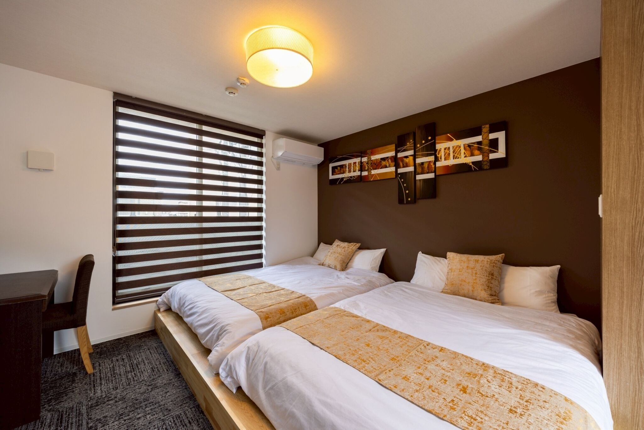 A hotel room with two beds, a desk, and a large window with blinds.